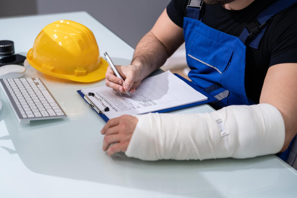 A man with a cast on his arm is writing on a clipboard, illustrating steps to take after a workplace injury.
