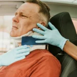 A doctor examines a man in a car, discussing whiplash injuries from a recent car accident